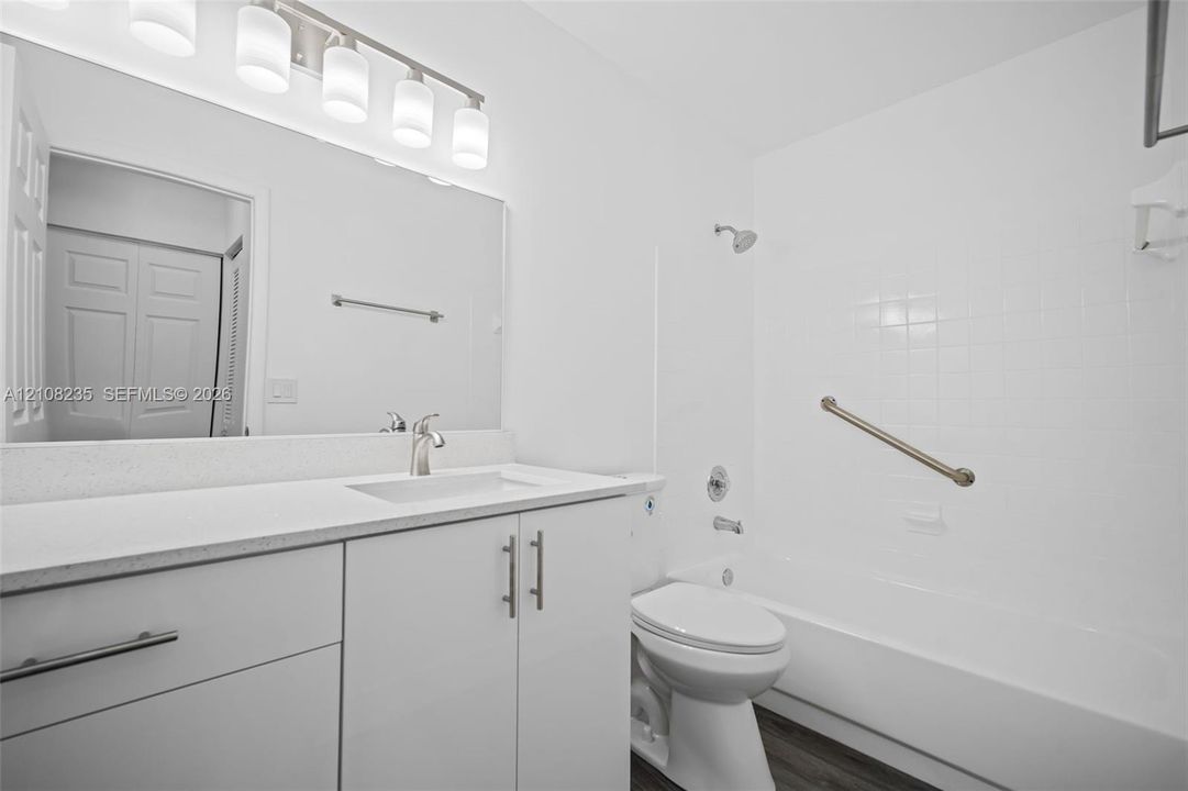 Bathroom featuring a white vanity with a solid surface countertop, an integrated sink, a full-width mirror, five-light overhead fixture, and a tile-surround shower and tub combination