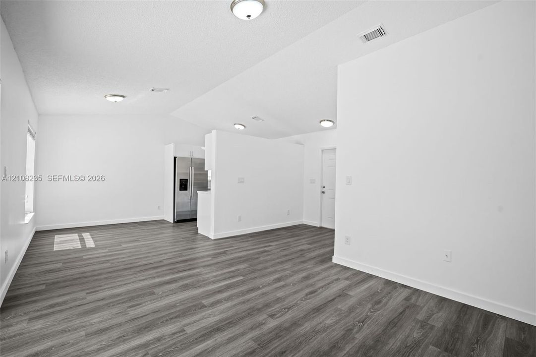 Vaulted ceiling with flush-mount lighting and wood-finish flooring throughout the open-concept space, featuring a stainless steel side-by-side refrigerator