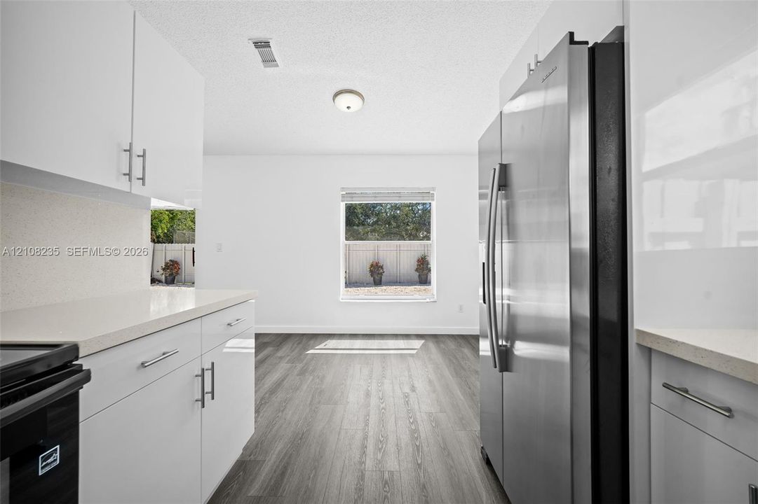 Kitchen featuring white flat-panel cabinetry, light-toned stone-surface countertops, wood-finish flooring, and a stainless steel side-by-side refrigerator