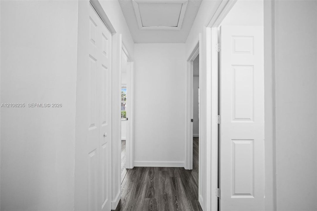 Hallway featuring wood-finish flooring, six-panel interior doors, and a ceiling access panel