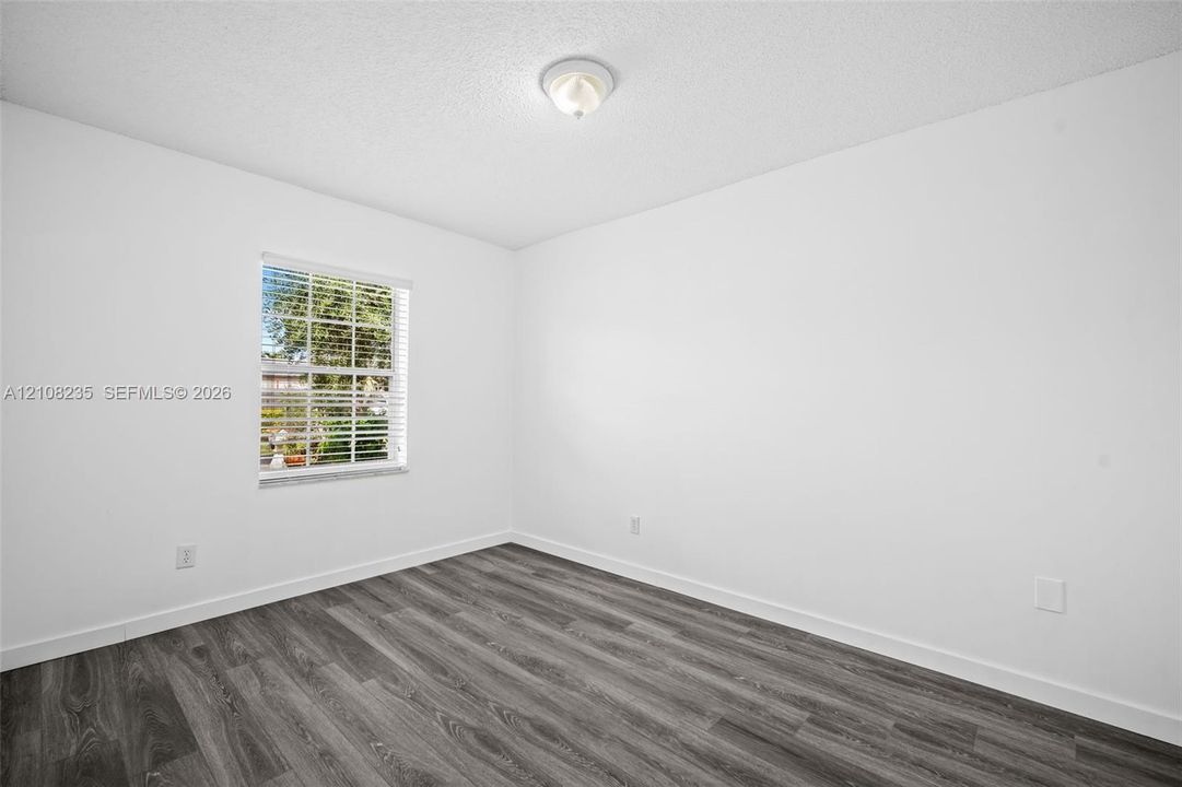 Room featuring wood-finish flooring, white walls, and a window with horizontal blinds