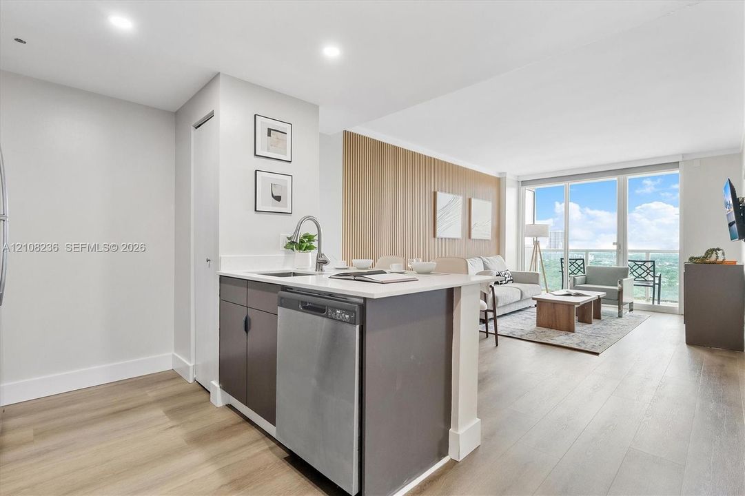 Kitchen featuring a peninsula with stainless steel dishwasher, white countertop, and high-arc faucet, complemented by wood-finish flooring, floor-to-ceiling windows, and a wood-slat accent wall