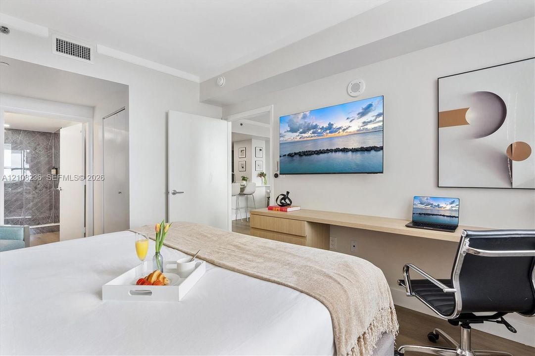 Built-in wall-mounted desk with light-finish cabinetry, wood-finish flooring, and wall-to-wall mirror paneling