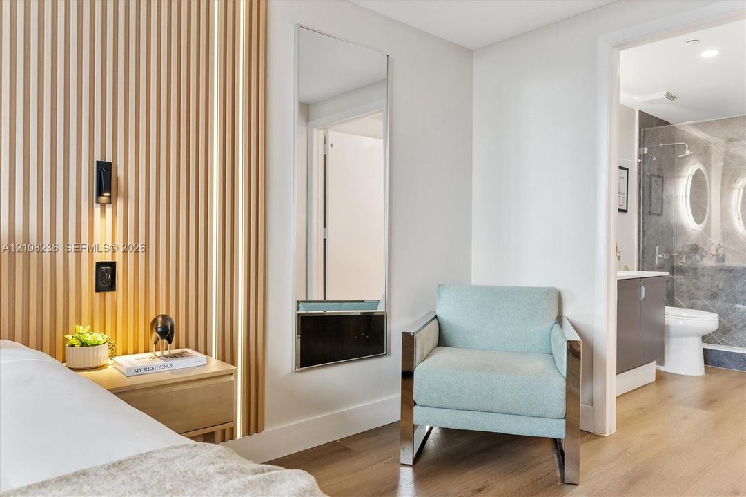 Vertical wood-slat accent wall with integrated linear lighting, wood-finish flooring, full-length wall mirror, and attached wall-mounted lighting fixture