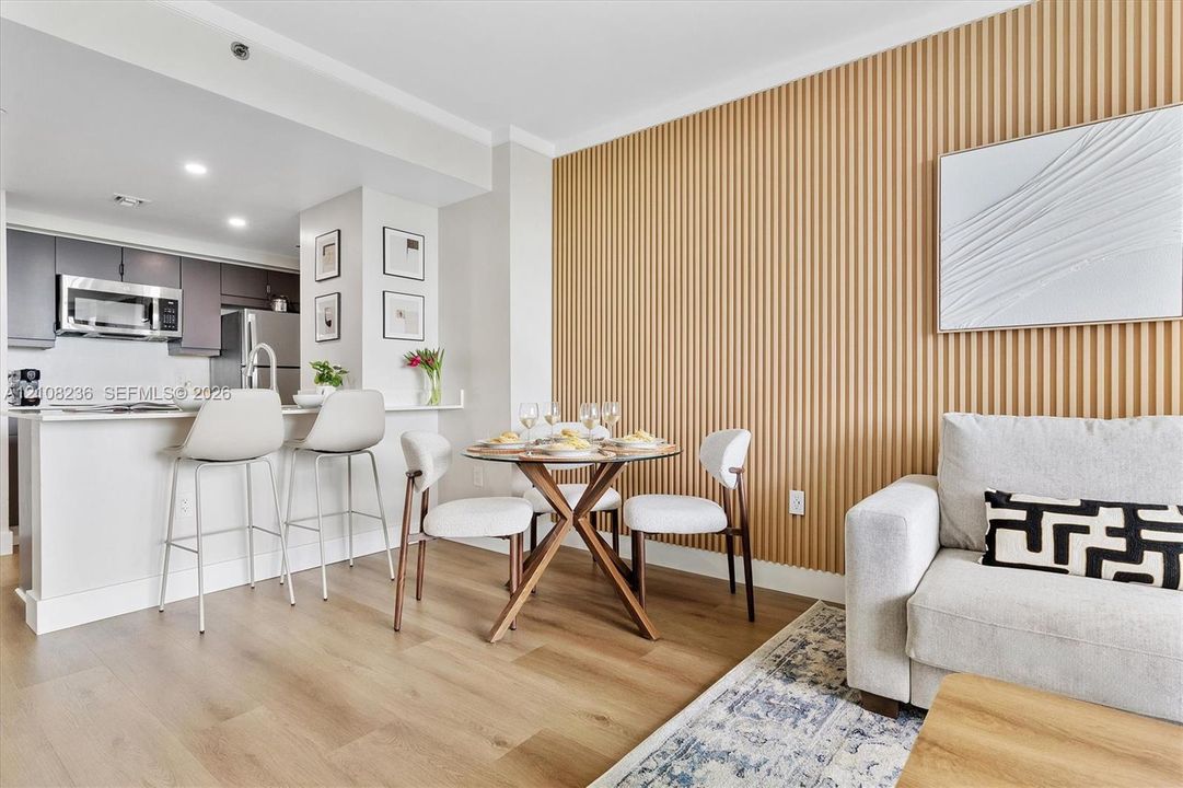Vertical slat wood-finish accent wall, wood-finish flooring, and kitchen featuring dark cabinetry, stainless steel appliances, and a quartz countertop breakfast bar