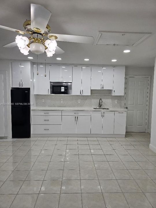 Glossy white cabinetry with modern hardware, stone-finish countertops, recessed ceiling lighting, tiled flooring, and a multi-light ceiling fan