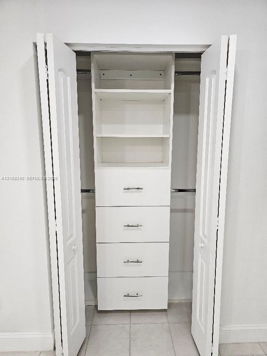 Closet featuring white bi-fold doors, integrated shelving, four drawers with metallic hardware, and dual clothing rods
