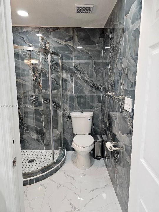 Bathroom featuring floor-to-ceiling dark-veined wall tile, a corner glass-enclosed shower with a mosaic-tile basin, and large-format white tile flooring with veining detail