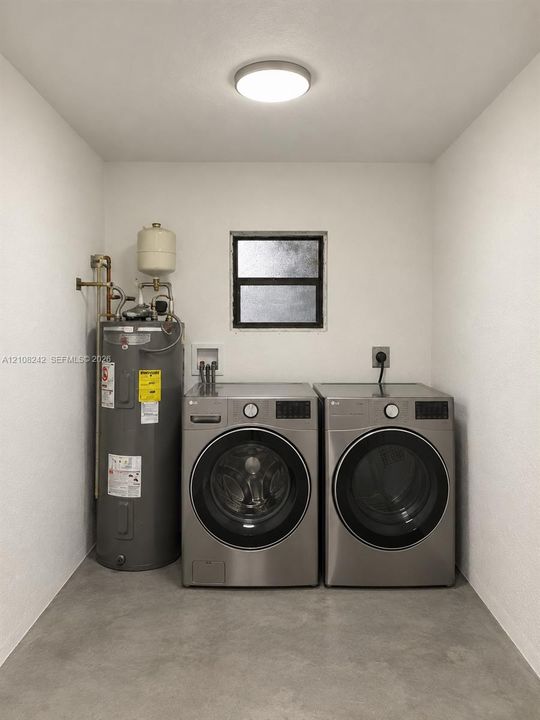 Utility space featuring a water heater, dual-stackable appliance connections, a single-hung window, and concrete flooring