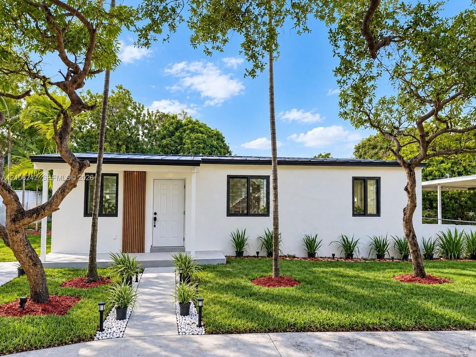 Stucco exterior featuring vertical wood-slat accent paneling, a dark metal roof, black-framed windows, and a paved walkway with stone borders