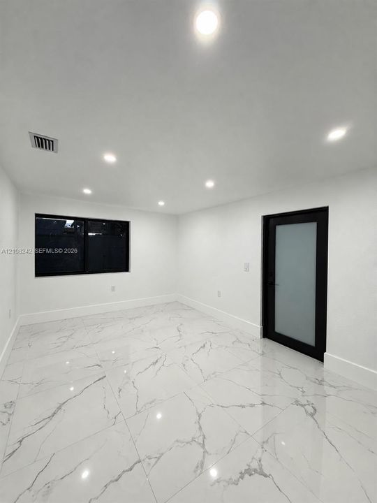 Polished large-format tile flooring with vein detailing, recessed ceiling lighting, and a modern door featuring a frosted glass panel and black frame