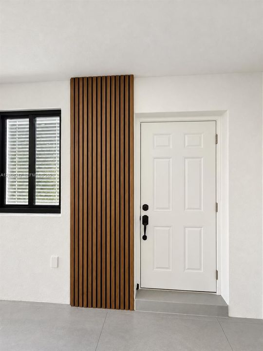 Vertical wood-slat accent wall, six-panel entry door with matte black hardware, black-framed window, and neutral large-format floor tiling