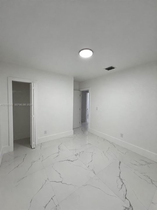 Neutral-toned interior space featuring large-format white stone-finish tile flooring with grey veining, a flush-mount circular ceiling light, and a built-in closet with bi-fold doors