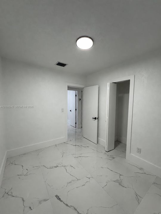 Large-format stone-style tile flooring with veining, solid-core interior doors, matte black hardware, and a flush-mount LED ceiling fixture