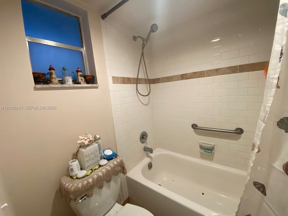 Bathtub with white subway tile surround, decorative tile inlay, adjustable shower head, and wall-mounted grab bar, complemented by a stone-finish window sill