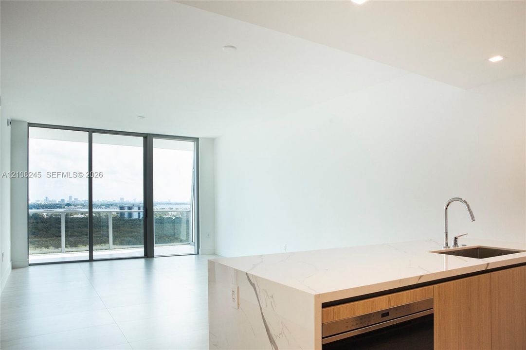 Open-concept kitchen featuring an island with stone-finish countertops, undermount stainless steel sink, and wood-finish cabinetry, complemented by floor-to-ceiling glass sliding doors and recessed lighting