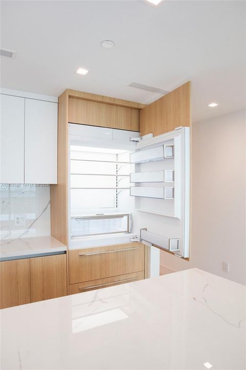 Integrated panel-ready refrigerator, custom wood-finish cabinetry, solid-surface countertop with veining, and recessed lighting