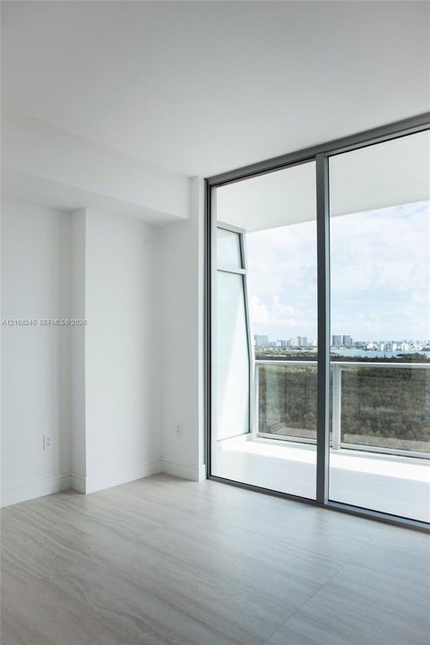 Floor-to-ceiling windows, wood-finish flooring, and a glass-paneled balcony