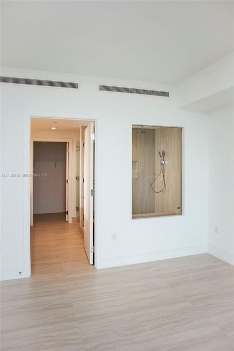 Wood-finish flooring, glass-enclosed shower stall with neutral tile surround, and recessed ceiling lighting