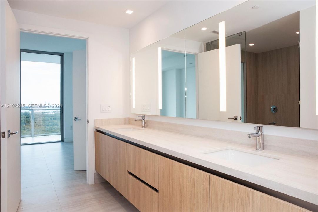 Floating vanity with wood-finish cabinetry, dual undermount sinks, light-toned stone countertop, integrated vertical LED mirror lighting, and polished chrome fixtures