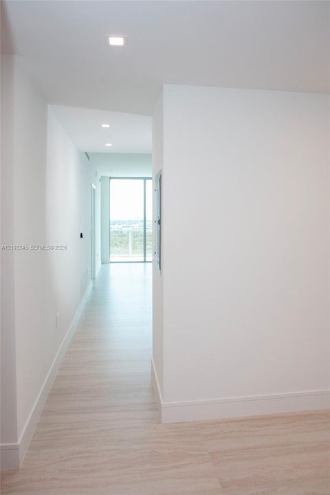 Hallway featuring light-toned flooring, recessed ceiling lighting, and floor-to-ceiling glass paneling