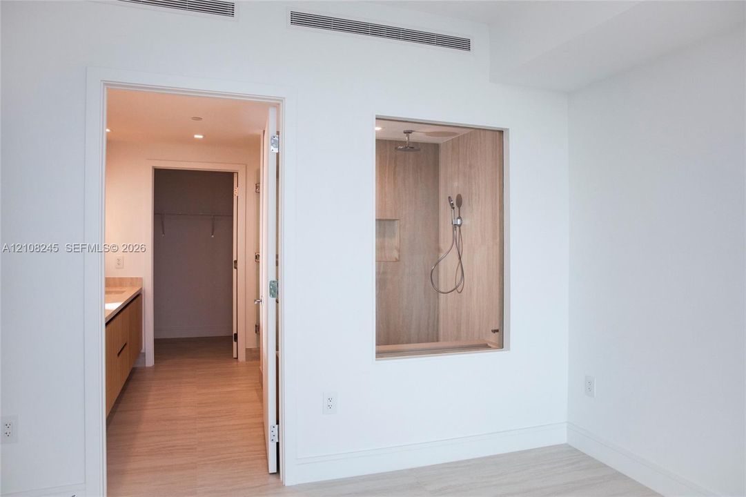 Shower enclosure with a glass partition, wall-mounted shower head, and built-in wall niche, featuring wood-finish wall tile and wood-finish flooring
