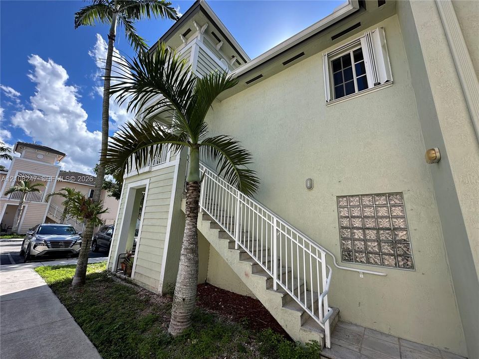 Multi-story exterior featuring light-toned stucco siding, metal-railing stairwell, glass block accent window, and exterior wall-mounted lighting