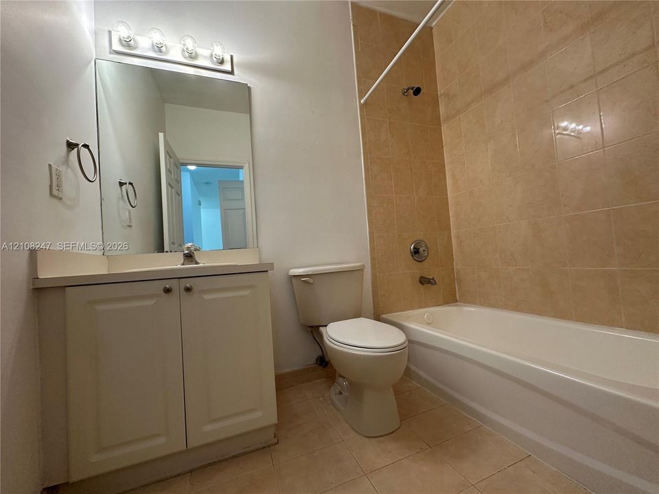Bathroom featuring a vanity cabinet with a countertop basin, a wall-mounted mirror with a four-light fixture, and a tub with tiled surround