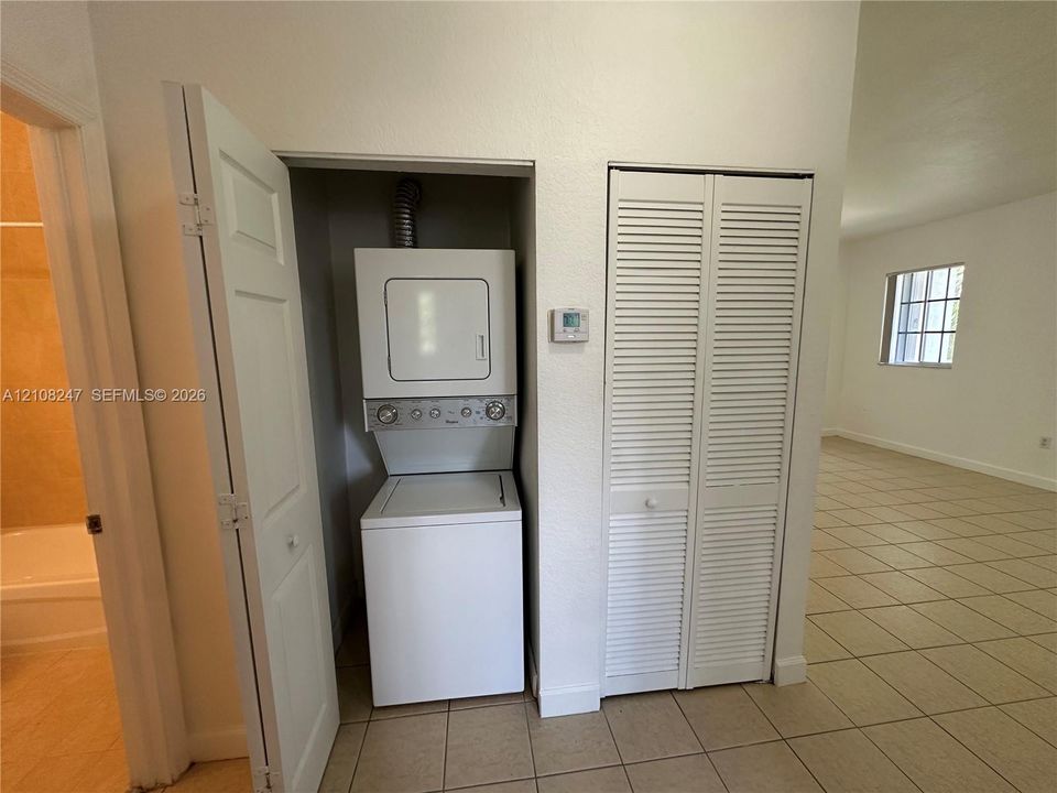 Laundry closet featuring a stackable washer and dryer unit, louvered bi-fold doors, and tile flooring