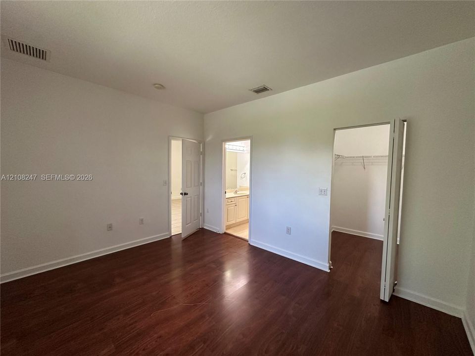 Room featuring wood-finish flooring, two six-panel interior doors, and a walk-in closet with built-in wire shelving