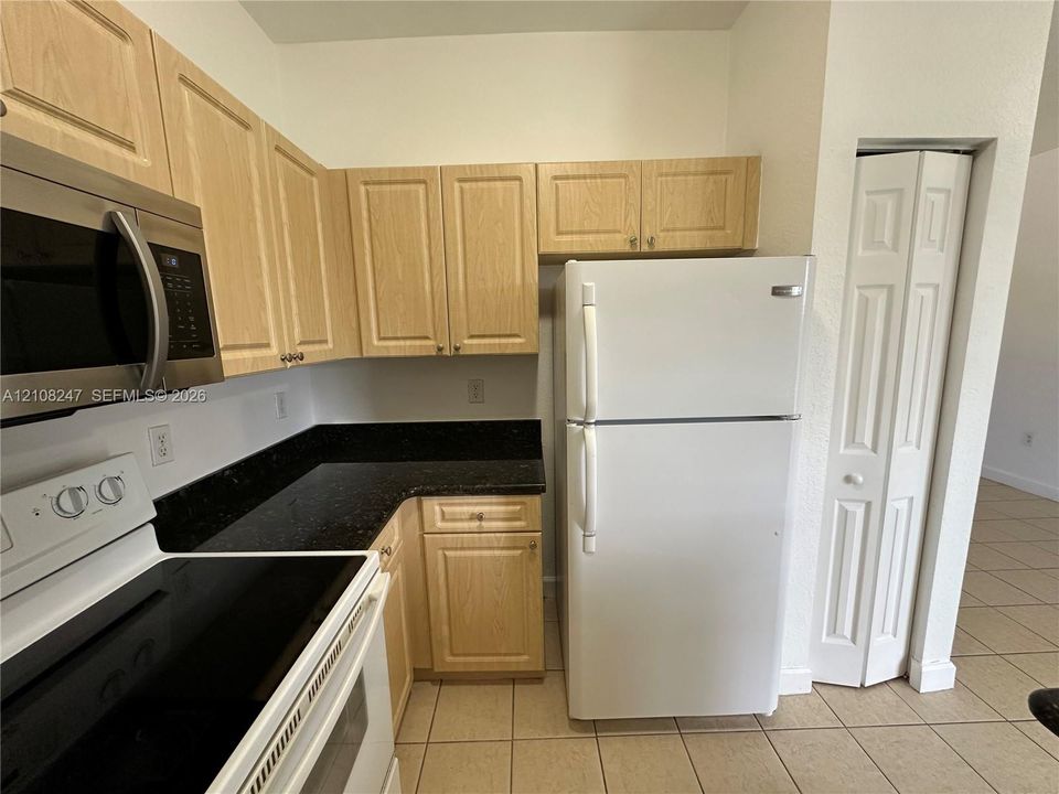 Kitchen featuring light-finish cabinetry, dark stone-style countertops, white appliance suite, and ceramic tile flooring