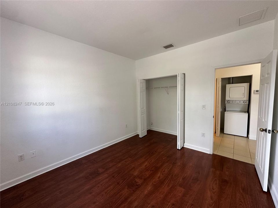 Room with wood-finish flooring, bi-fold closet doors, and attached utility area featuring a stacked laundry unit