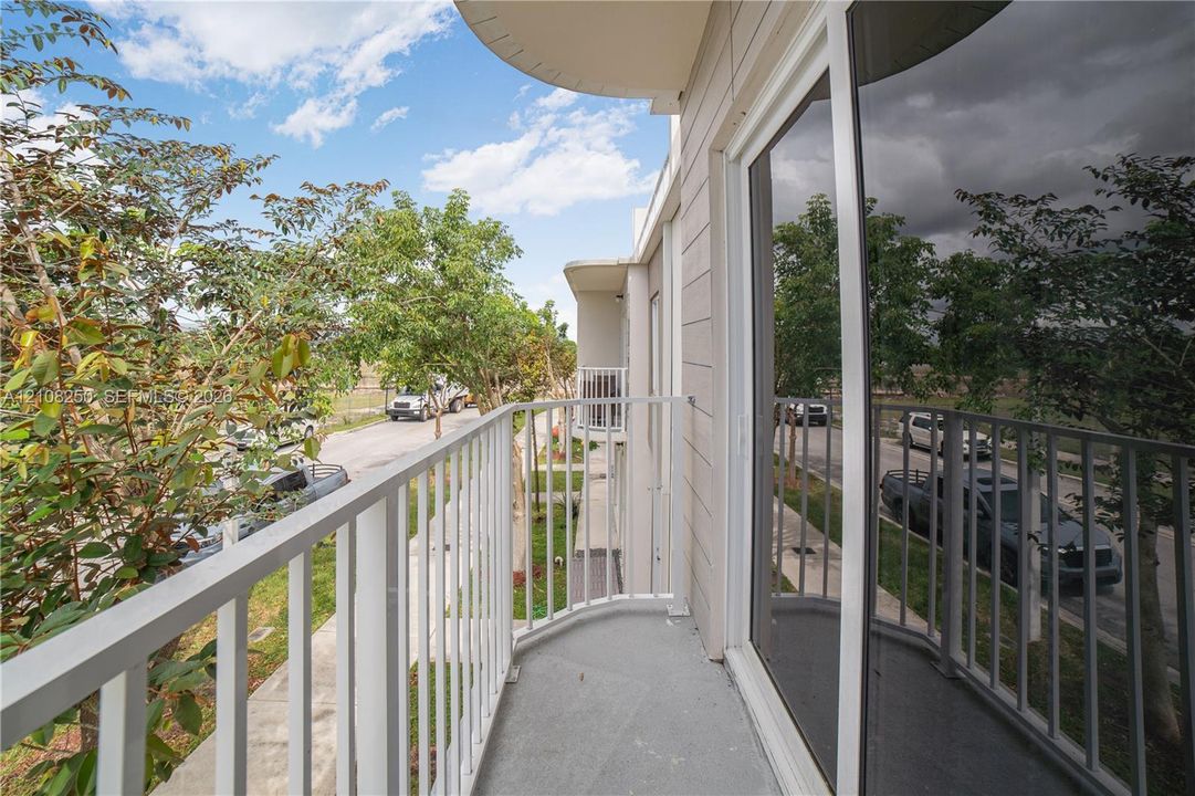 Exterior balcony with a curved metal railing, concrete flooring, and full-height sliding glass door