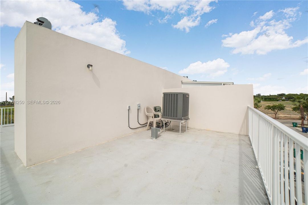 Open-air rooftop terrace featuring a concrete floor, white metal railings, and stucco wall finish