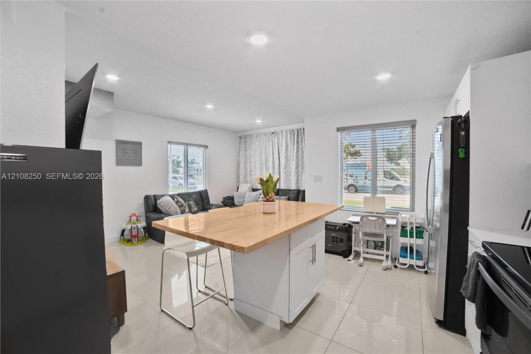 Kitchen featuring a center island with a wood-finish countertop, white cabinetry, recessed lighting, and large-format tile flooring