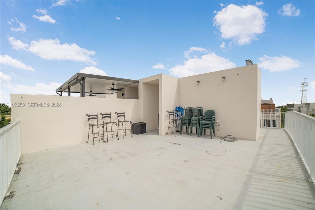 Rooftop terrace featuring a covered pavilion, integrated ceiling fans, stucco perimeter walls, and white metal railing