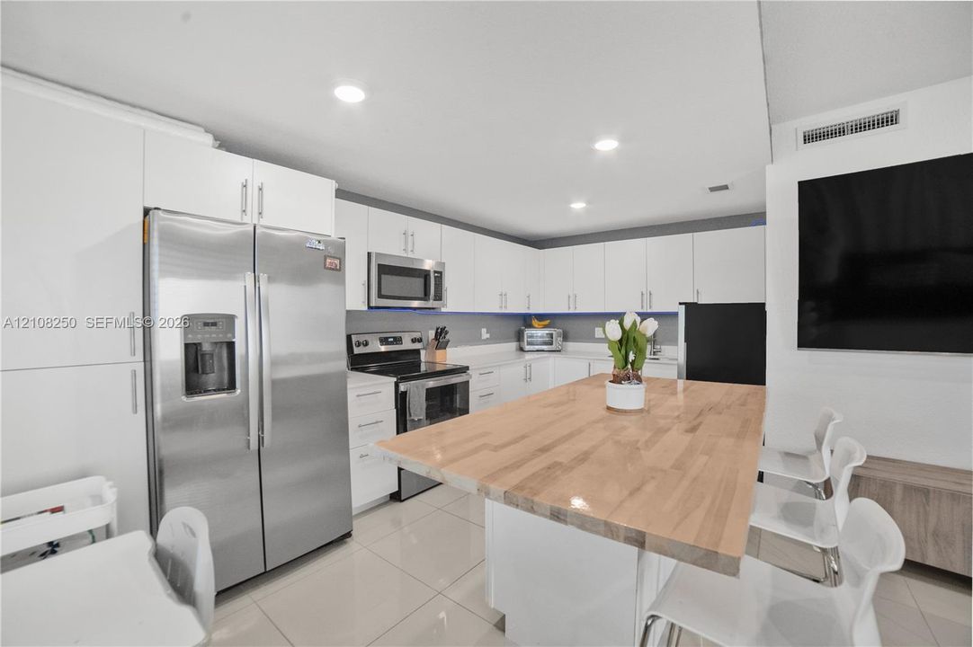 Kitchen featuring white cabinetry, stainless steel appliances, butcher block kitchen island, and tile flooring
