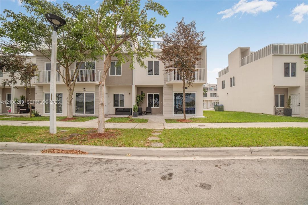 Modern multi-story exterior featuring a neutral stucco facade, second-floor balconies with metal railings, and ground-level covered patio spaces