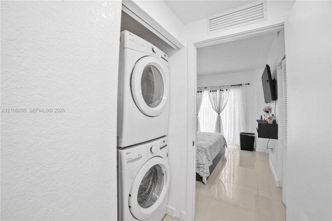 Laundry closet featuring a white stacked washer and dryer unit, high-gloss tile flooring, and louvered closet doors