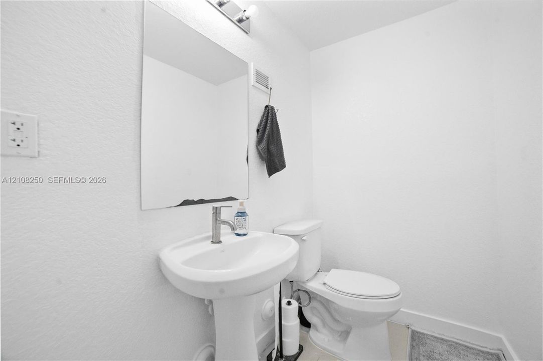 Pedestal sink with a single-handle chrome faucet, rectangular wall-mounted mirror, and standard-height toilet