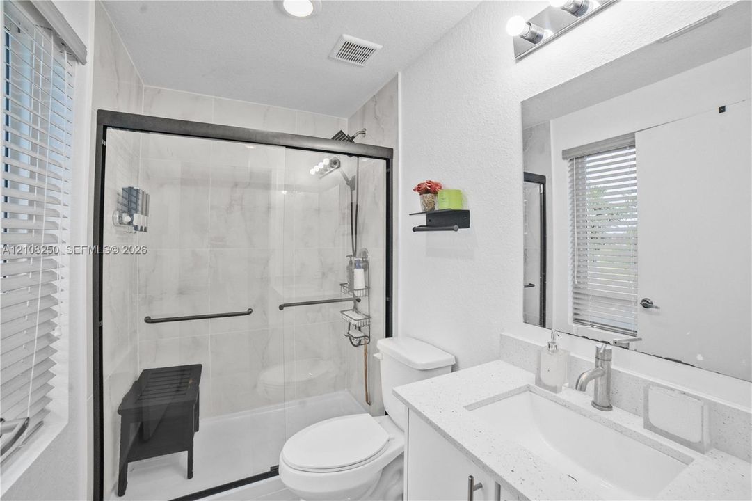 Bathroom featuring a shower with a sliding glass door, tiled surround, and integrated bench, accompanied by a vanity with a stone-composite countertop and a large wall-mounted mirror