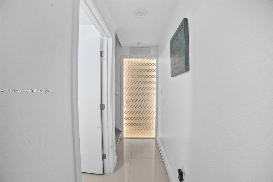 Hallway featuring polished tile flooring, recessed ceiling lighting, and a geometric-patterned backlit decorative panel
