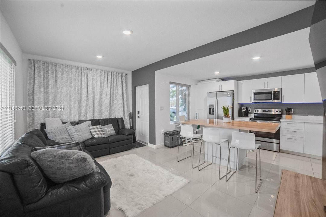 Kitchen featuring white flat-panel cabinetry, stainless steel appliances, a wood-surface breakfast bar, recessed lighting, and large-format tile flooring