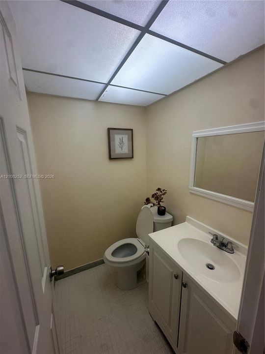 Bathroom featuring a white vanity with an integrated basin, a framed wall mirror, a tiled floor, and a drop ceiling
