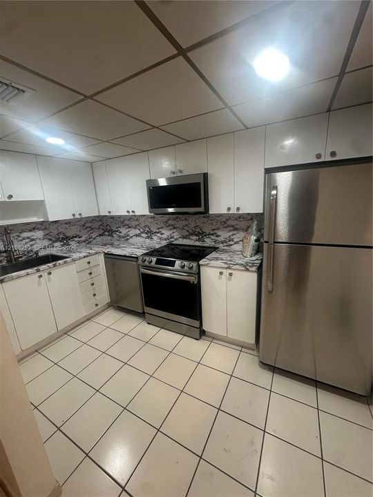 Kitchen featuring white cabinetry, stainless steel appliances, patterned stone-style countertops, and tile flooring