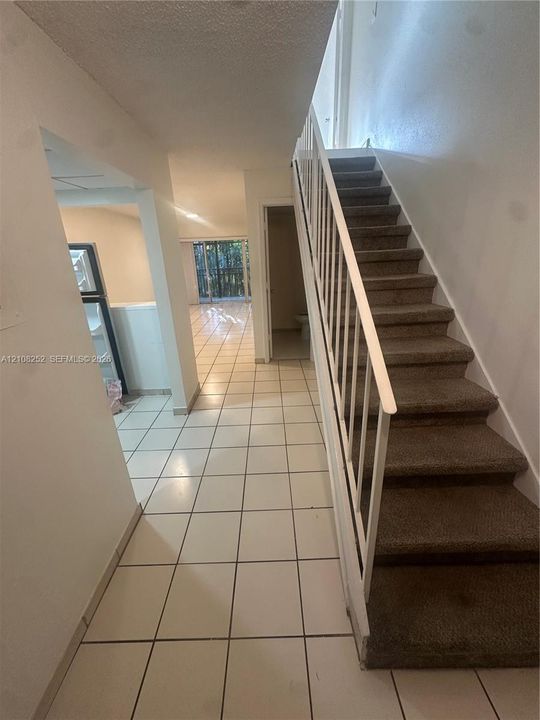 Interior hallway featuring white ceramic tile flooring and a carpeted staircase with a white metal railing