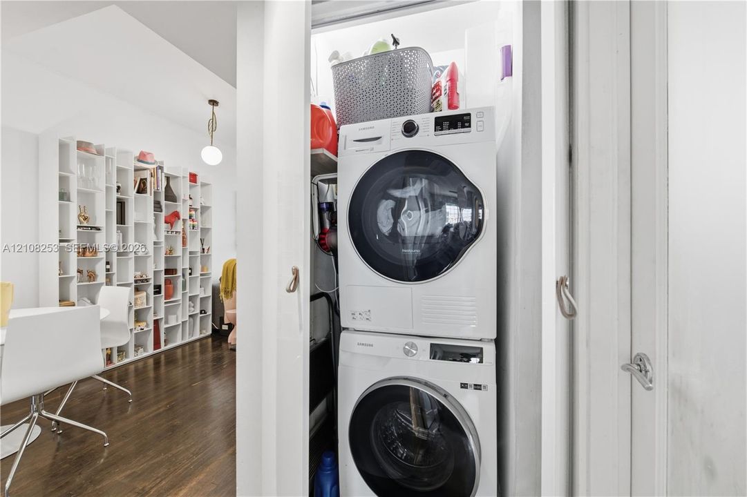 Stacked laundry center featuring a front-load washer and dryer set, white built-in shelving, and wood-finish flooring