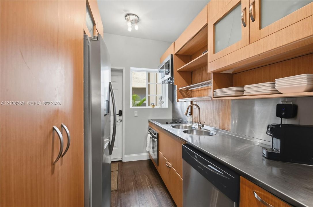 Galley kitchen featuring wood-finish cabinetry, stainless steel countertops, integrated stainless steel appliances, and wood-finish flooring