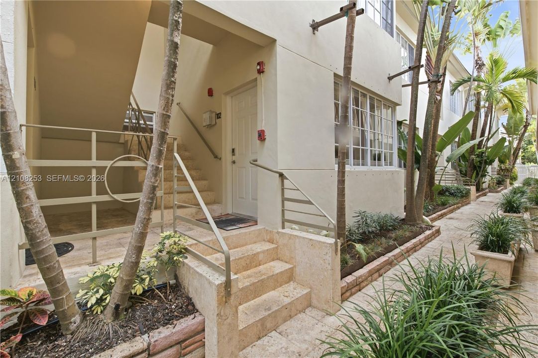 Exterior walkway featuring natural stone pavers, concrete stairs, metal handrails, and built-in landscape planters with mature palms and shrubbery