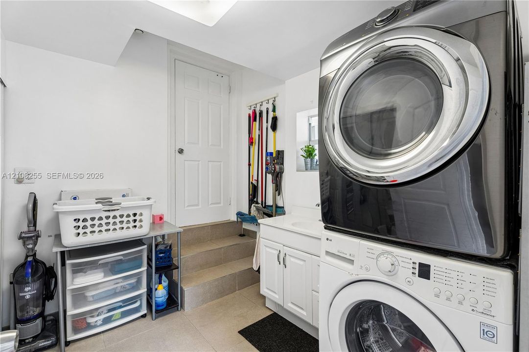 Laundry area featuring a stacked washer and dryer, white shaker-style cabinetry, an integrated basin sink, and tiled flooring